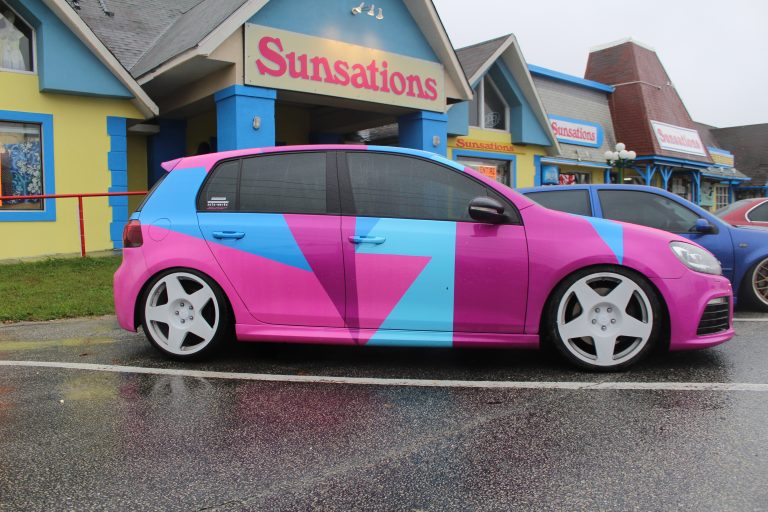 Custom pink and blue wrapped Volkswagen Golf with white rims parked outside Sunsations store.