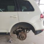 Picture of a white german SUV on a hydraulic stand with it's wheel off.