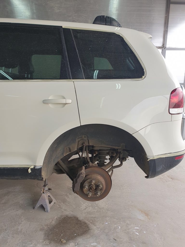 Picture of a white german SUV on a hydraulic stand with it's wheel off.